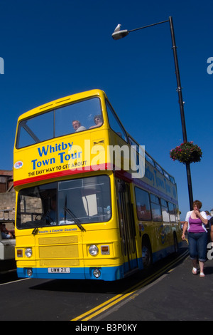 A bright yellow open topped double decker bus taking tourists on a tour around the seaside town of Whitby North Yorkshire UK Stock Photo