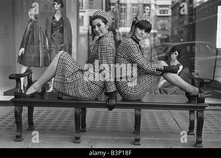 Fashions taken during London Fashion Week 1964 Two piece suit with matching hats two models sitting on a bench back to back posing for the camera Stock Photo