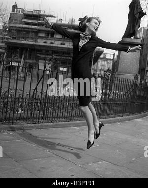 Fashions taken during London Fashion Week 1964 Knee length dress with long sleeves jumping for joy in front of railings and a large building factory Stock Photo