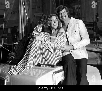 Man and woman posing together on a boat he is wearing a washable safari jacket with matching trousers She i swearing acrylic jersey in stripes January 1975 fashion models couple smiling men mens women womens 1970s mirror reveille 24 1 75 peter isbell Stock Photo