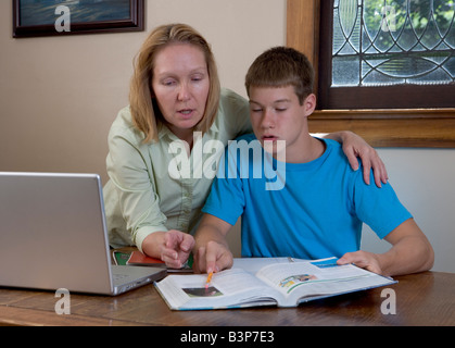 A mother helps her teen-aged son with his school homework with a laptop open, perhaps using the internet as a tool. Stock Photo