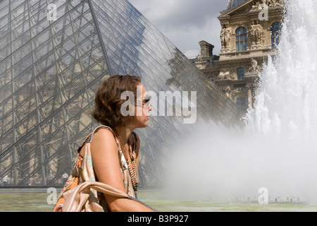 Seated young woman, admiring the fountains,  in front of the The Louvre, Paris, France Stock Photo