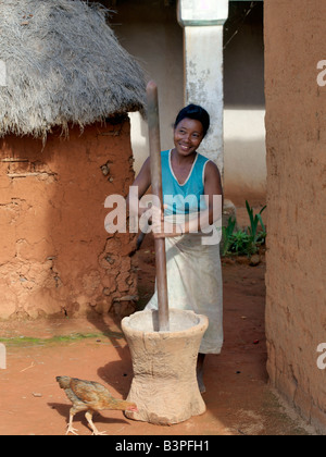 Madagascar, Southern Highlands, Andohatangona. A Malagasy woman grinds corn using a wooden pestle and mortar at an attractive Ma Stock Photo