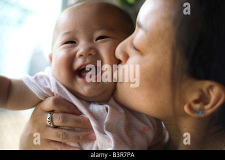 japanese mother kissing smiling six month old baby girl close up at home Stock Photo