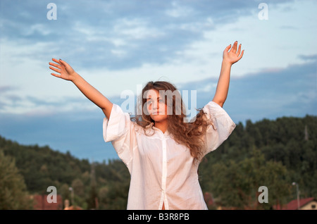 Portrait of a young woman 16 18 outdoors with arms raised looking away Stock Photo