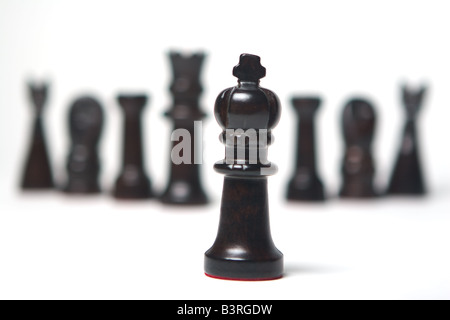Set of black dark wood hand carved chess pieces isolated on white background selective focus on king in front of other pieces Stock Photo