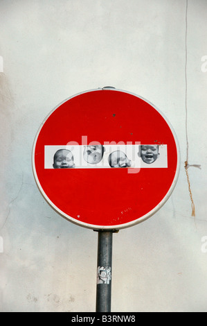 A No Entry sign against a whitewashed wall with pictures of a smiling baby face on it. Stock Photo