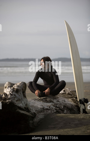 Surfer sitting on log on beach, Cox Bay near Tofino, British Columbia, Canada Stock Photo