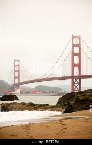 Vertical view of the Golden Gate Bridge viewed from Baker Beach with container ship passing underneath Stock Photo