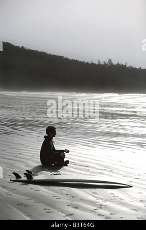 Surfer meditating on beach, Cox Bay near Tofino, British Columbia, Canada Stock Photo