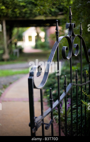 Iron gateway leading into a beautiful garden courtyard with ivy trellis and white gazebo in the background. Stock Photo