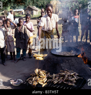 Tanzania, A woman deep-fries small tilapia fish caught in Lake Rukwa, Southwest Tanzania, before sending them to market in Mbeya, which is the commercial centre of the fertile Southern Highlands region. Lake Rukwa is a long, narrow lake lying in a basin of inland drainage southeast of Lake Tanganyika; it forms part of the Western Rift. The lake is very shallow (maximum depth not much more than twenty feet)) and mildly alkaline. Any change in its water level causes great fluctuations of its size. Stock Photo