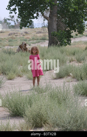 Young mixed race girl in pink dress standing in the desert before a cottonwood tree Stock Photo