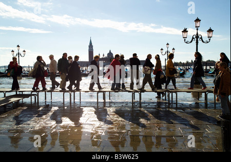 Tourists in silhouette walking on raised platforms to avoid the flooding on the pavement over looking Bacino di Siant Marco. Stock Photo