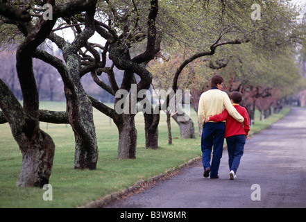 Married couple walking arm in arm down a tree lined road in a country park Stock Photo