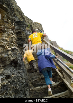 A dad and his two children climbing the steep steps up to Tintagel Castle in Cornwall, England UK Stock Photo