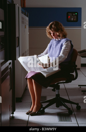 Female office worker inspects print outs in a corporate computer room Stock Photo