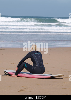 Female surfer sat on her surfboard in a wetsuit watching the waves Stock Photo