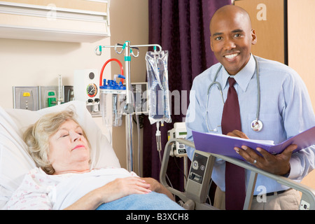 Doctor Making Notes About Senior Woman Lying In Hospital Bed Stock Photo