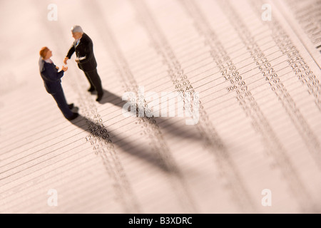 Figurines Of Two Businessmen Shaking Hands On A Financial Newspaper Stock Photo