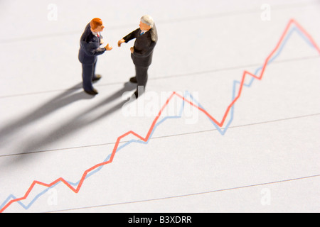 Figurines Of Two Businessmen Shaking Hands On A Line Graph Stock Photo