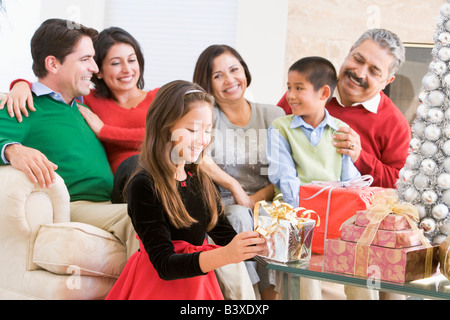 Family Sitting On Sofa In Front Of Christmas Presents, Young Girl Selecting A Gift Stock Photo