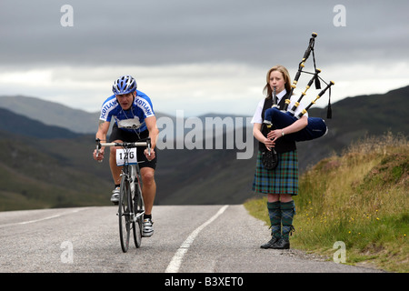 Cyclist on racing bike passes a piper on the B862, Great Glen Way around Loch Ness, Scottish Highlands, Scotland, UK Stock Photo