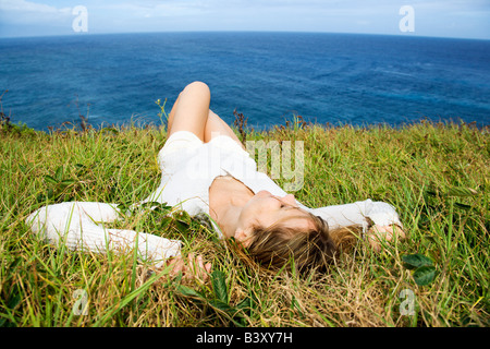 Portrait of young redheaded woman relaxing in grass above the ocean in Maui Hawaii Stock Photo