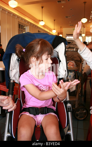 three year old girl with muscular dystrophy signing butterfly in stroller, talking to friend in a restaurant Stock Photo