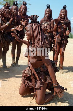 Namibia, Kaokoland. Himba women perform the otjiunda dance, stamping their feet, clapping and chanting while one of them sways o Stock Photo