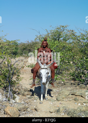 Namibia, Kaokoland. A Himba mother and child ride home on a donkey. Their bodies gleam from a mixture of red ochre, butterfat an Stock Photo