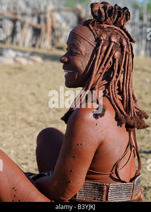 Namibia, Kaokoland. An old Himba woman relaxes outside her home. Her body gleams from a mixture of red ochre, butterfat and herb Stock Photo