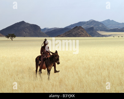 Namibia, Kaokoland. An old Himba woman, upright despite her years, rides her donkey through harsh land where mid-day temperature Stock Photo