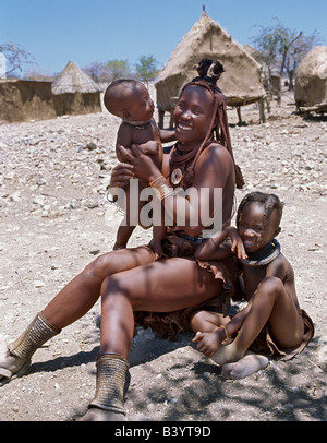 Namibia, Damaraland, Palmwag. A Himba mother and children in traditional attire. Their bodies gleam from a mixture of red ochre, Stock Photo