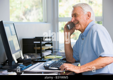 Man in home office on telephone using computer smiling Stock Photo