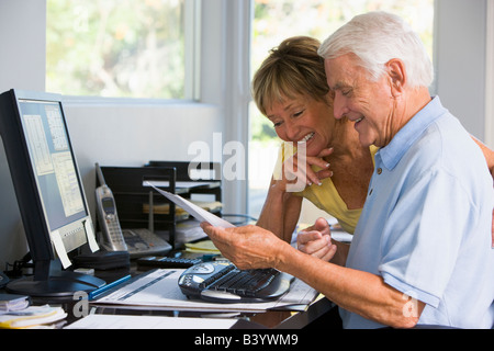 Couple in home office with computer and paperwork smiling Stock Photo