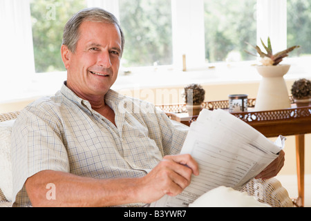 Man in living room reading newspaper smiling Stock Photo