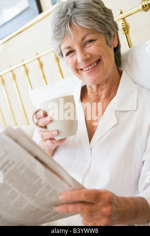 Woman in bedroom with coffee and newspaper smiling Stock Photo