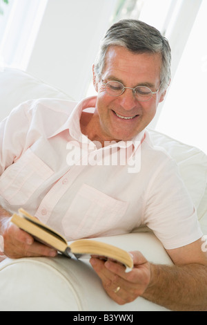 Man in living room reading book smiling Stock Photo