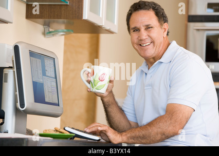 Man in kitchen with computer and coffee smiling Stock Photo