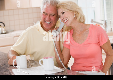 Couple in kitchen with coffee using telephone together and smiling Stock Photo