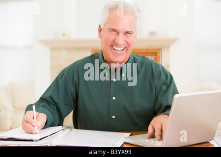 Man in dining room with laptop and paperwork smiling Stock Photo