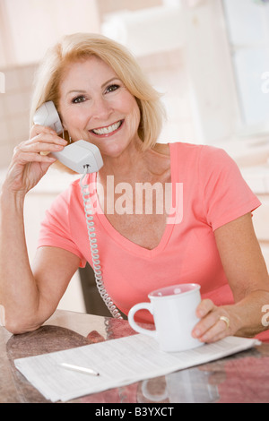 Woman in kitchen using telephone and smiling Stock Photo