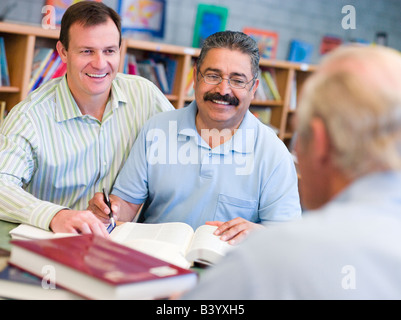 Two men sitting in library near another man with a book and notepad (selective focus) Stock Photo