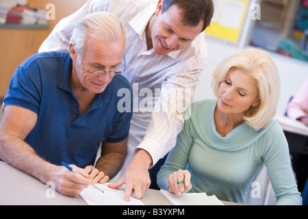 Adult students in class with teacher helping Stock Photo