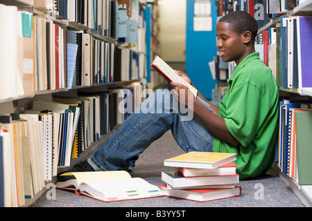 Man sitting on floor in library reading book Stock Photo