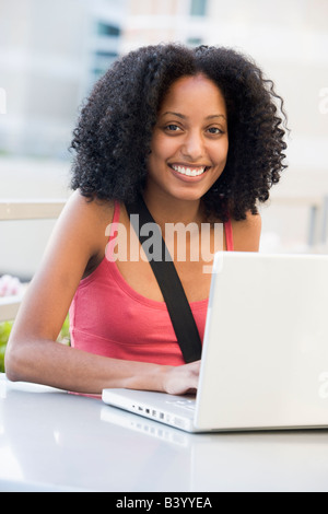 Woman sitting at table outdoors with laptop smiling (high key) Stock Photo