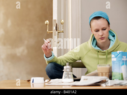 Young woman holding a cigarette while reading a newspaper Stock Photo