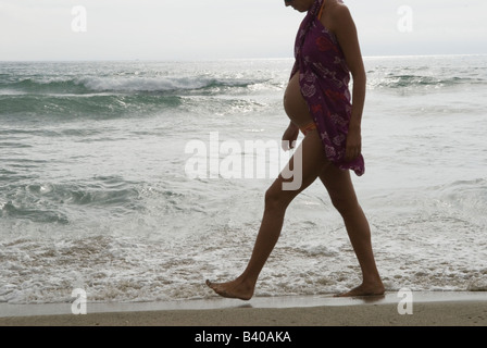 Pregnant woman walking along beach splashing up water wearing a blouse over a bathing costume. Canet Plage nr Perpignan South of France  2008 Stock Photo