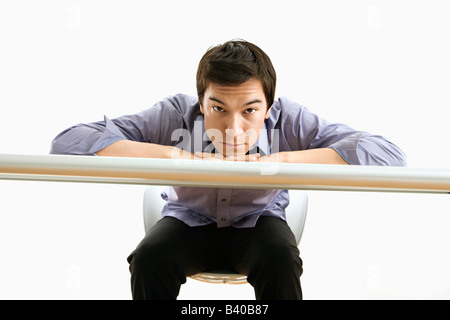 Young Asian business man with head on desk looking at viewer Stock Photo